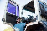 un camionero con una camisa azul mirando algo al costado de su camion de trabajo