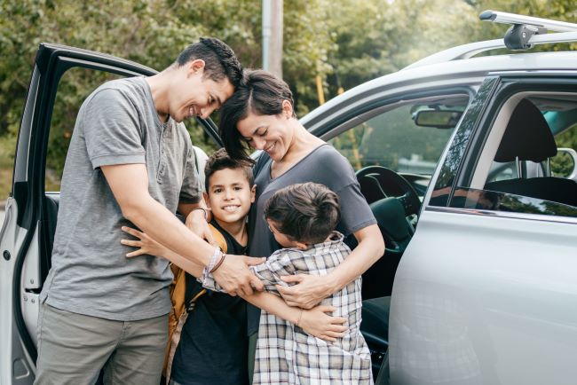 una familia abrazandose al lado de su auto