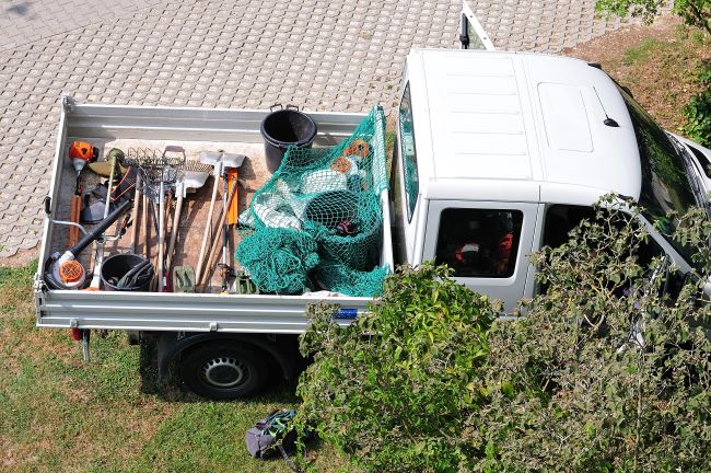 un camion de jardineria con herramientas en la parte trasera esta estacionado en un lugar de trabajo