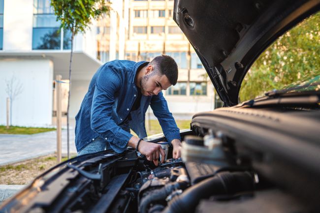 un joven trabajando en su auto mirando el motor