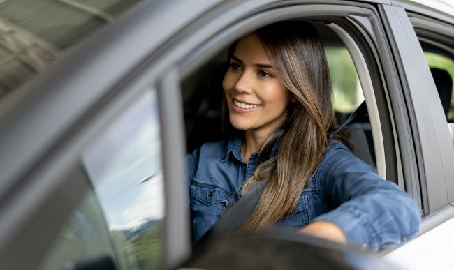 una senora sentada en su auto mirando algo a lo lejos