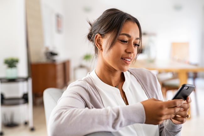 una mujer sentada en su sofa mirando su telefono