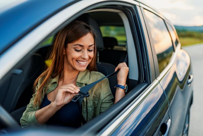 una mujer sentada en su auto negro poniendose el cinturon de seguridad para comenzar a conducir