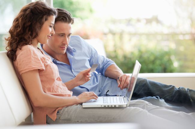 un hombre y una mujer sentados en el sofa mirando una computadora